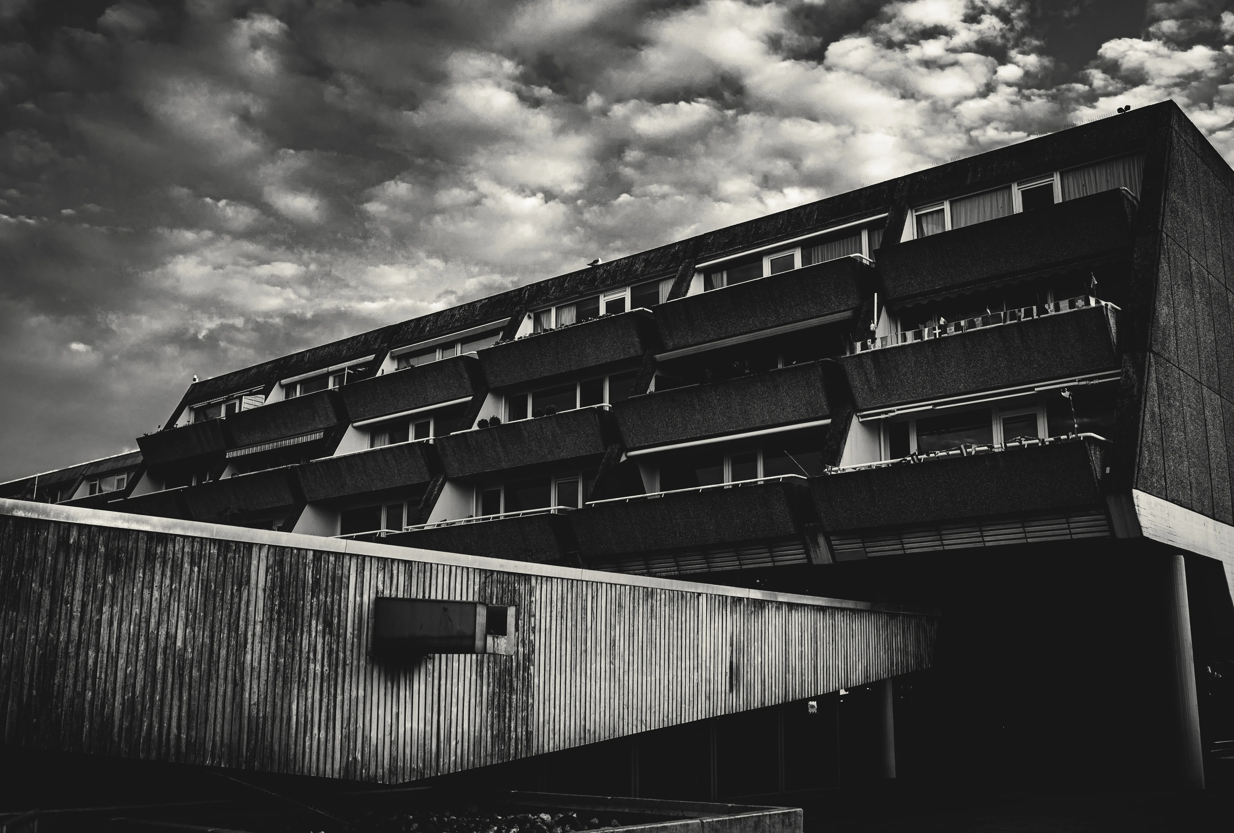 A black-and-white concrete brutalist building against a dramatic cloudy sky.