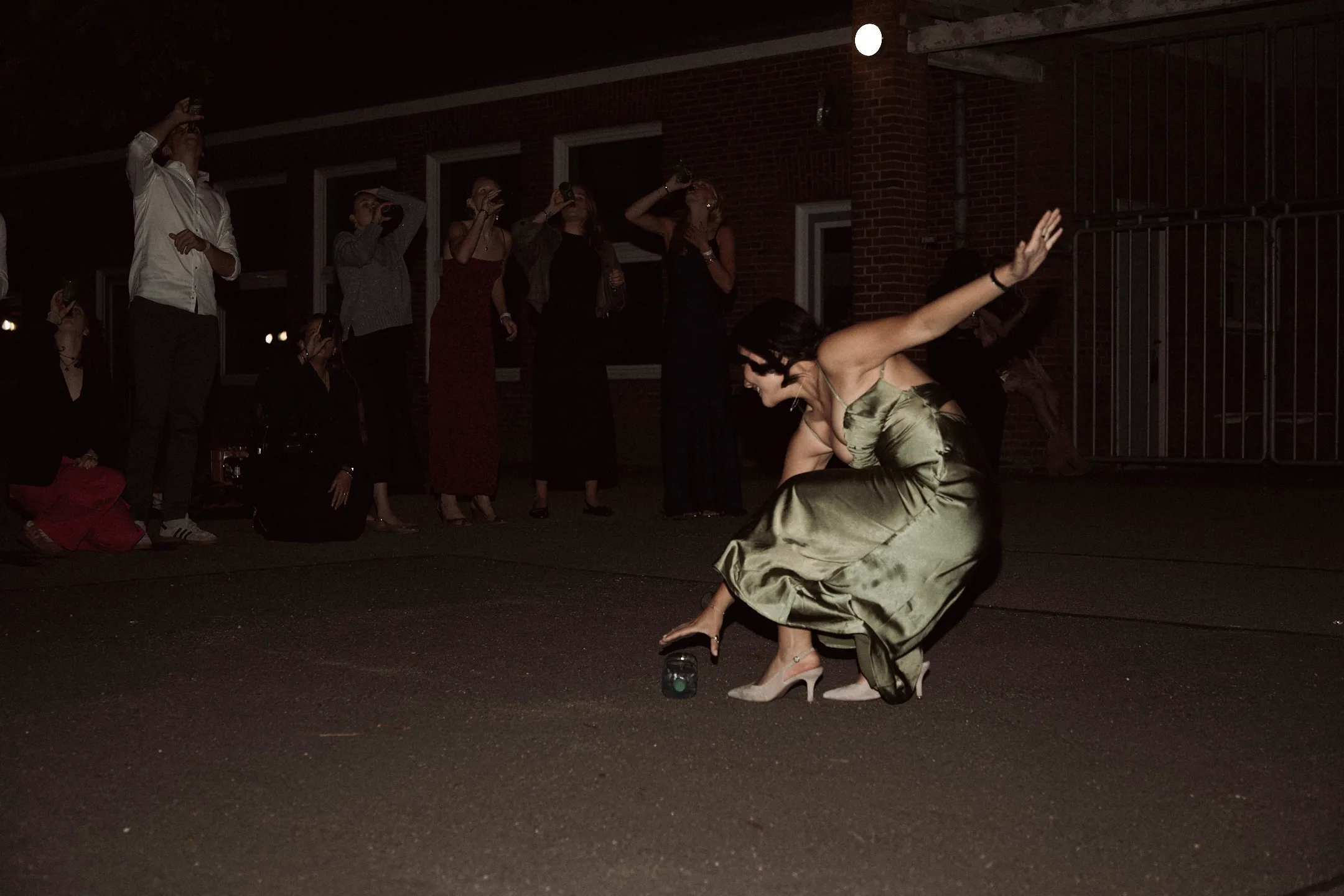 A figure in a green dress mid-motion on a dark street, onlookers behind.