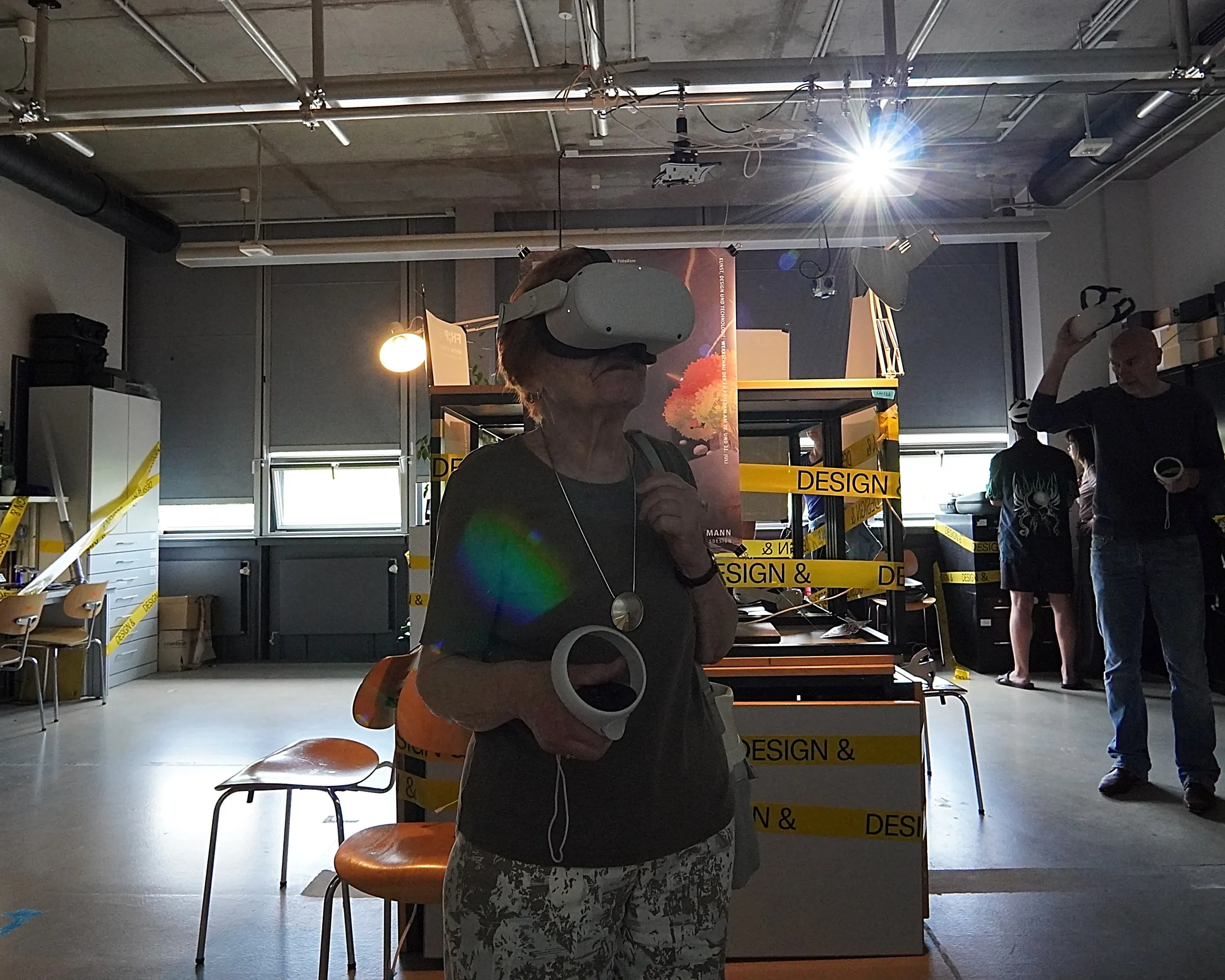 An older visitor wearing a VR headset, reaching out in a workshop space.